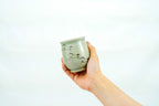 Hand holding a pale green Soma Eight Horses cup, showing its running horse pattern and small raised foot.