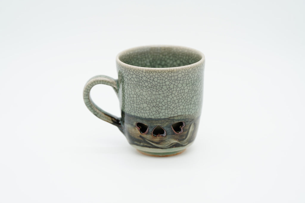 Rear view of the Soma mug with its handle on the left, showing plain crackle glaze and heart-shaped openings near the base.