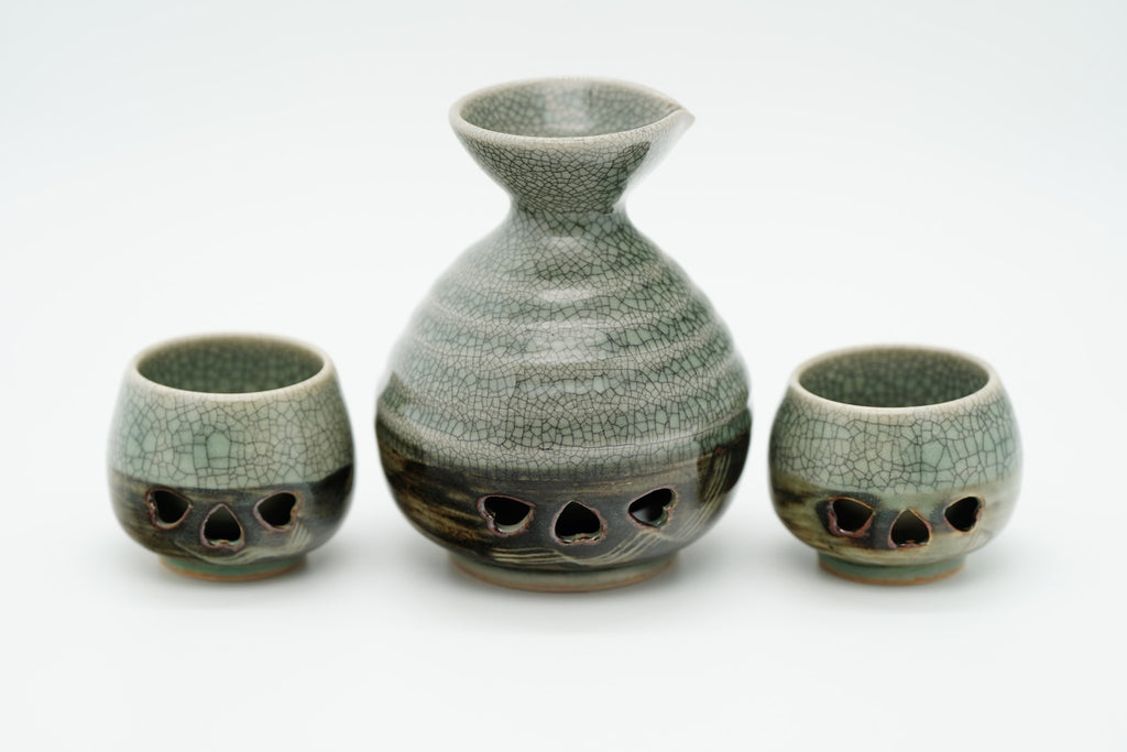Rear view of the Soma sake carafe and two cups showing crackled glaze and dark patterned lower sections.