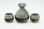 Rear view of the Soma sake carafe and two cups showing crackled glaze and dark patterned lower sections.
