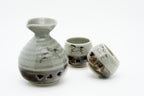 Angled view of the Soma sake carafe beside one upright cup and one tilted cup.
