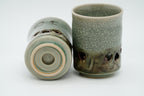 One Soma cup on its side showing a recessed base mark, beside an upright cup with crackled glaze and double walled heart shape.
