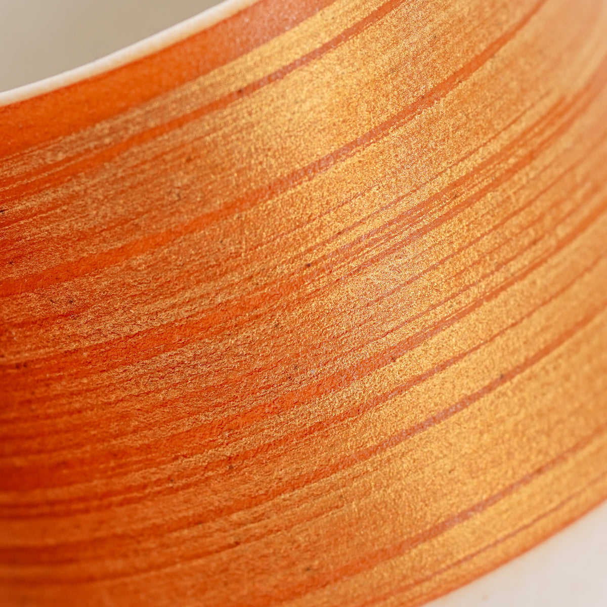 Close-up of fine gold brushstrokes across the KOUSYUHAI Vermilion & Gold cup’s vermilion surface beneath a white rim.