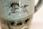 Close-up of the Soma mug’s running horse on grey-green crackle glaze above the dark lower band.