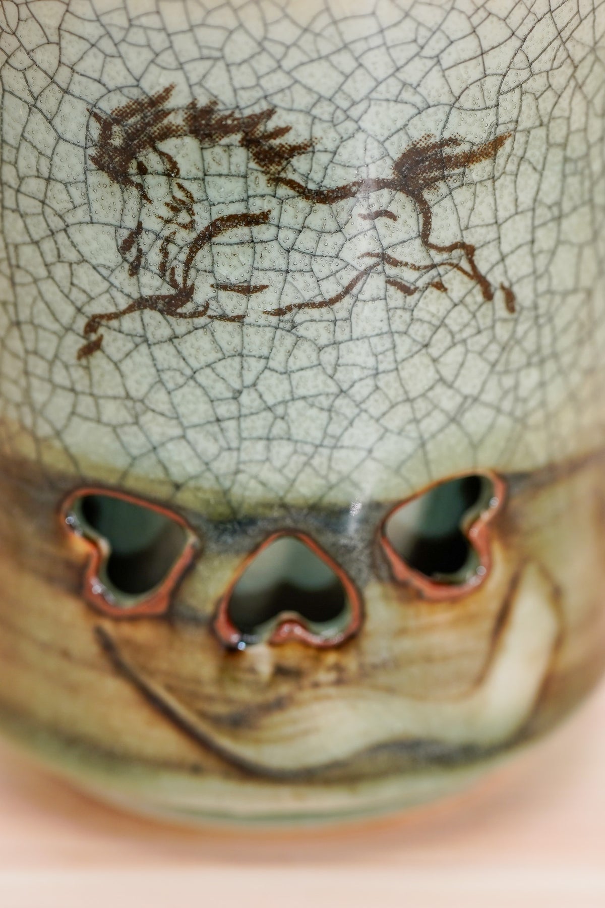 Close-up of a running horse on crackled grey-green glaze above three heart-shaped openings. Soma ware cup. 