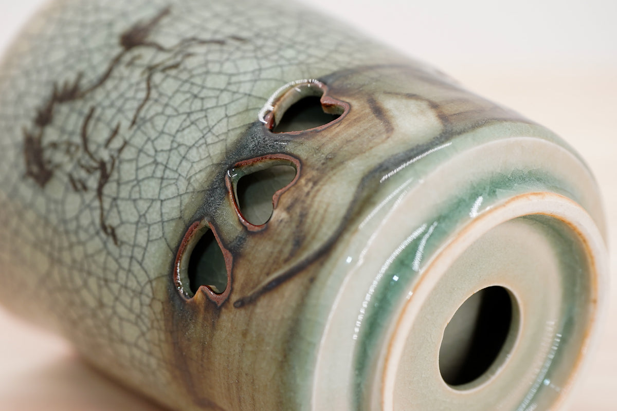 Close-up of heart-shaped openings and swirling brown and green glaze near a Soma cup’s base.