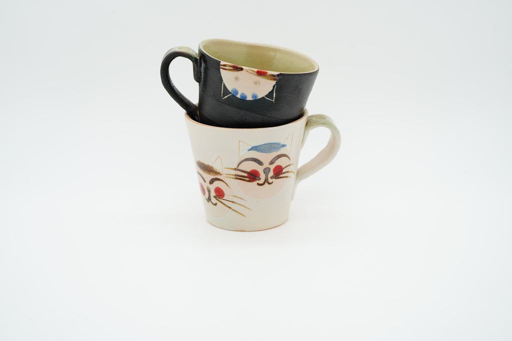 Black Couple Cats mug resting inside a cream mug, with the handles pointing in opposite directions.